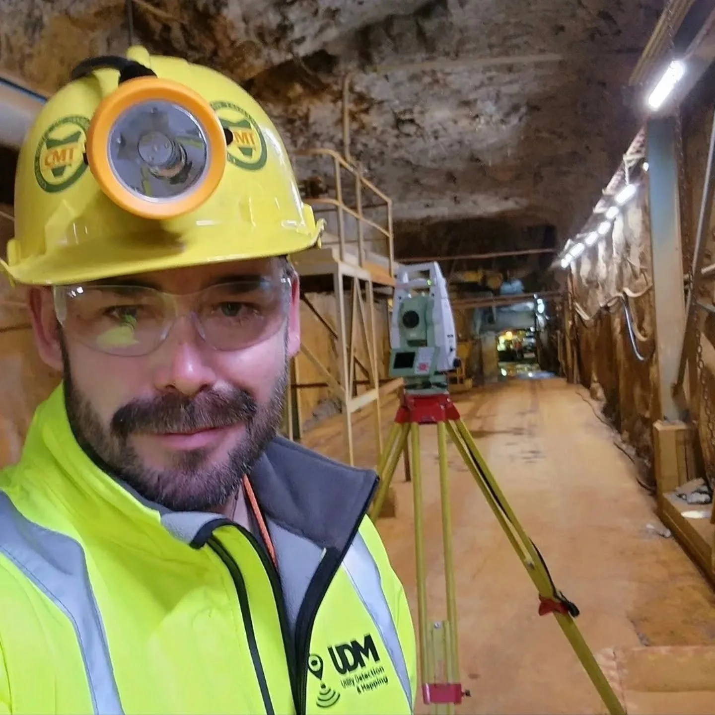 UDM surveyor in helmet and hi-vis working underground beside survey instruments